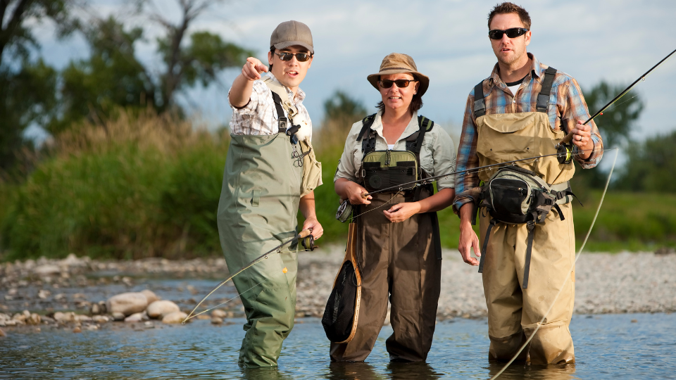 Fisherman wearing a sling pack while wading knee-deep in a flowing river