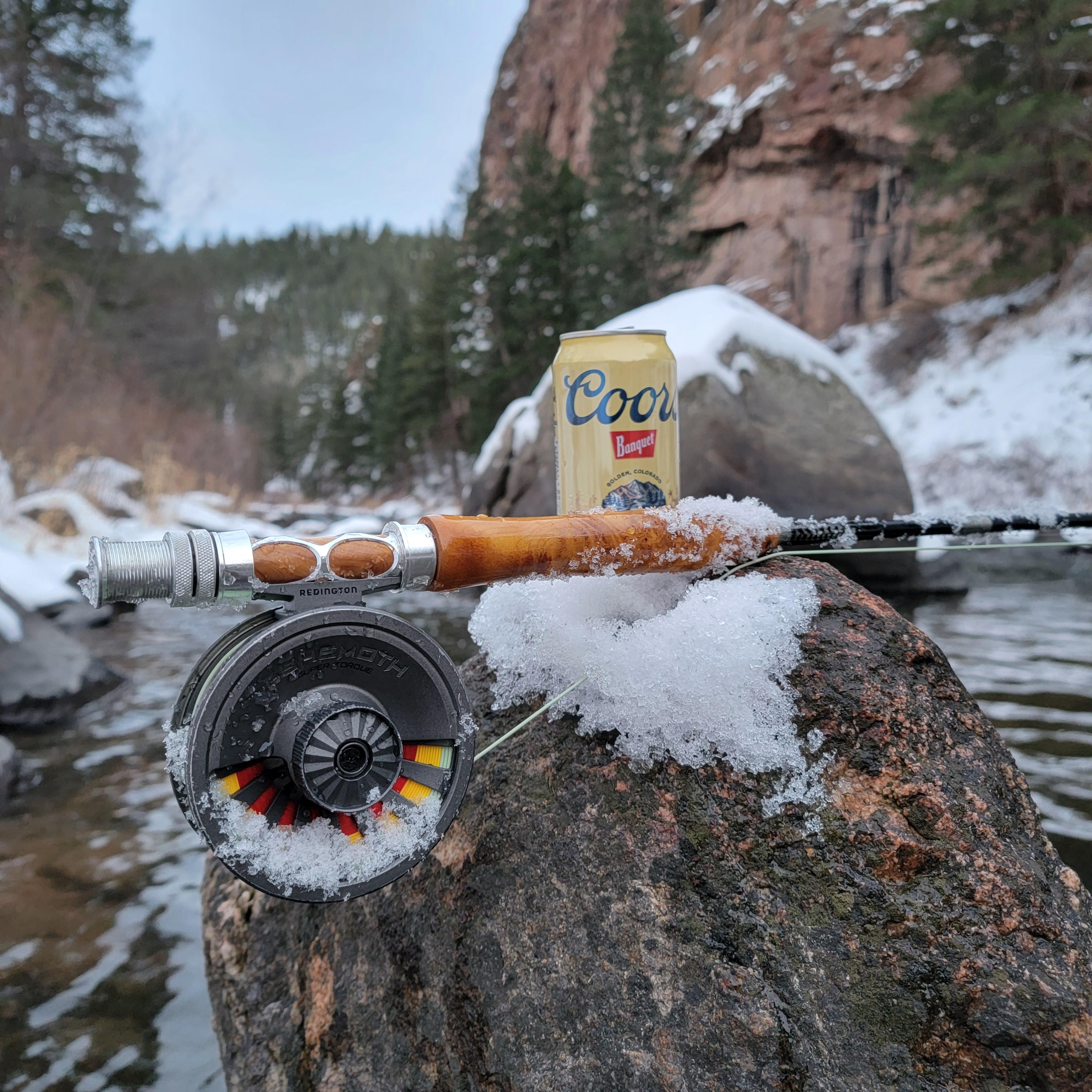 Rise Beyond Fly fishing company fly rod up close next to a can of coors beer and clear creek in coloraado