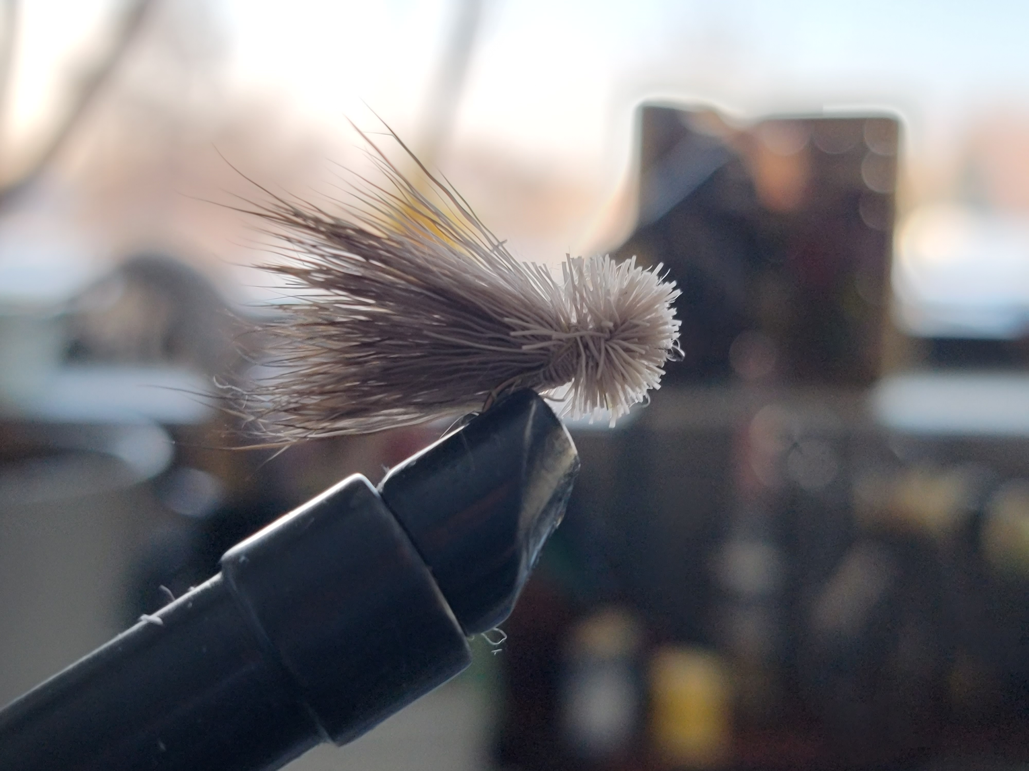 A close-up view of an Elk Hair Caddis fly, showcasing its wings made of elk hair, peacock herl body, and brown hackle feather. This popular fly pattern is commonly used for fly fishing