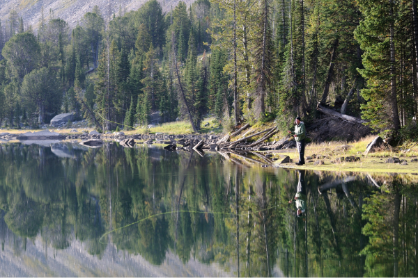 two men on a fly fishing boat together. One is oaring the boat and the other is standing on the bow fly fishing. The boat is off in the distance floating down the colorado river. 