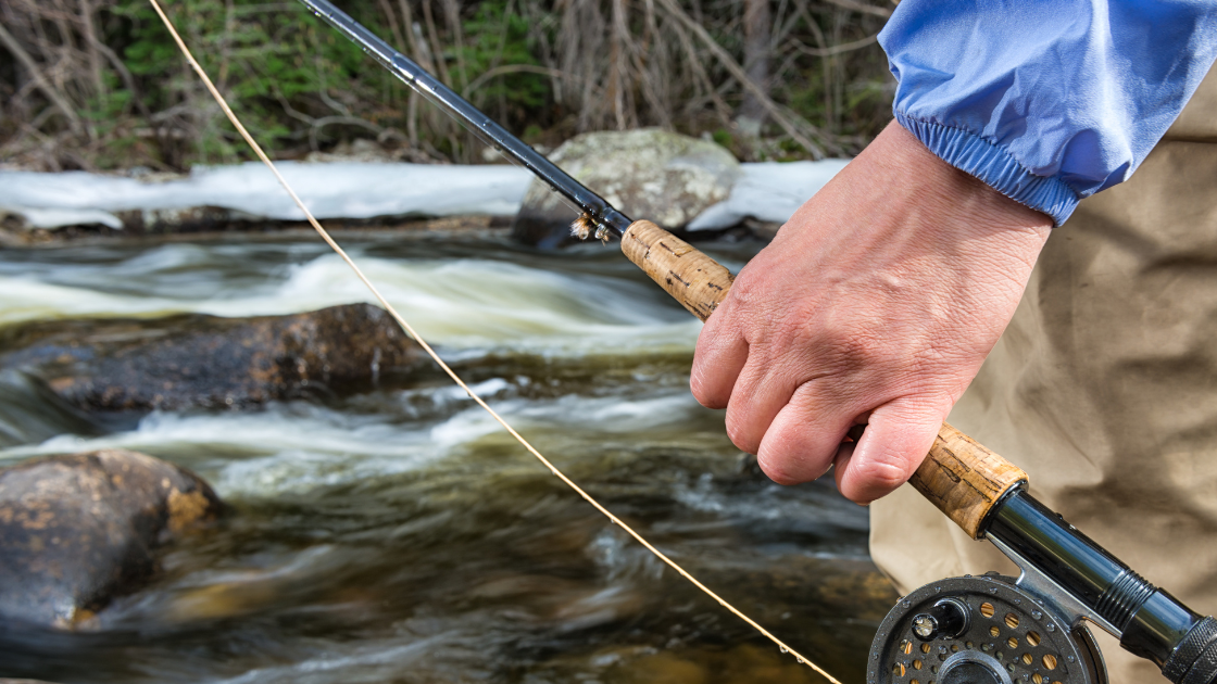 Fly fisherman casting on the Dolores River below McPhee Reservoir with rocky cliffs in the background.