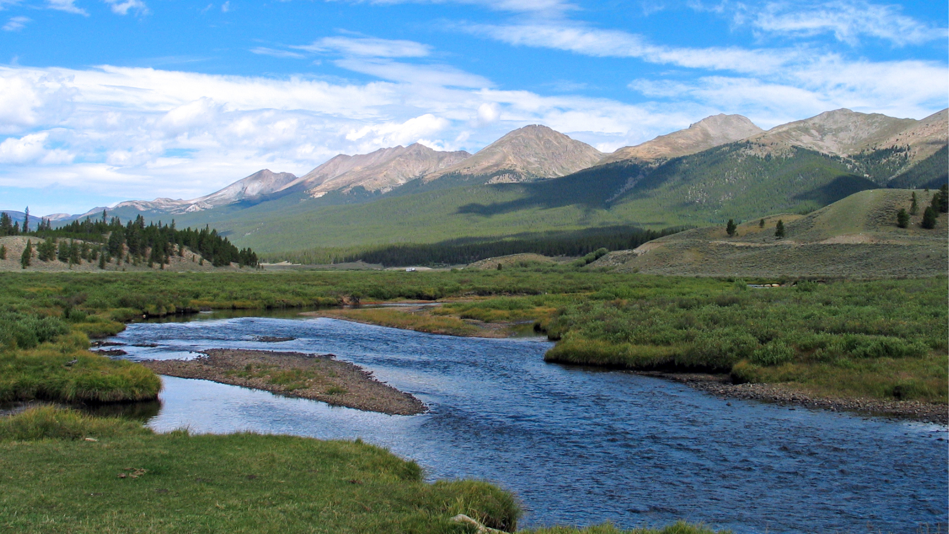 Colorado River high in Rocky Mountain National Park curving its way through the peaks. The river is surrounded by cool grass banks holding cutthroat trout