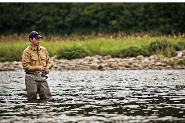 An angler fly fishing in a river, casting a line against a backdrop of flowing water and forested hills, benefiting from the physical activity