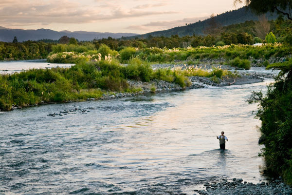 An angler casting a fly rod into a clear high-altitude lake in Colorado, surrounded by alpine peaks and forested shores.