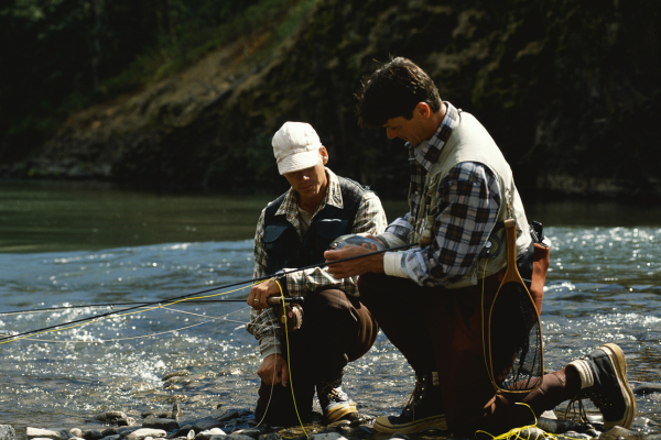 An angler standing in a river, carefully casting a fly rod into calm waters while focusing on technique.