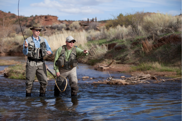 Volunteers participating in a river cleanup in Colorado, collecting debris along a scenic stream surrounded by trees and mountains.