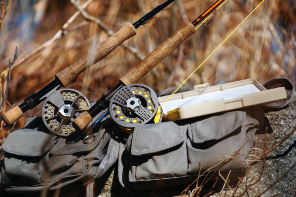 An organized fly fishing EDC setup with compact tools, flies, and a sling pack neatly arranged on the riverbank, ready for action